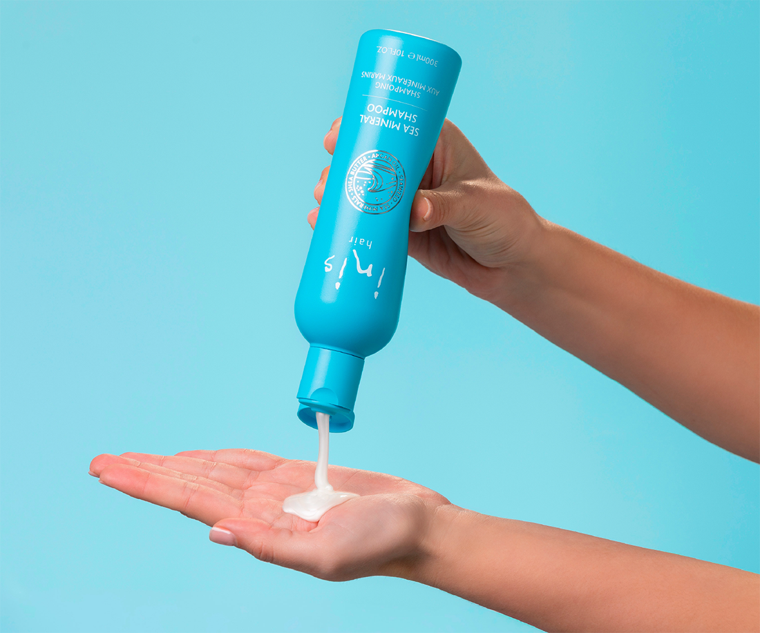 Person holding a blue bottle of Inis Shampoo and applying it to their hand against a light blue background