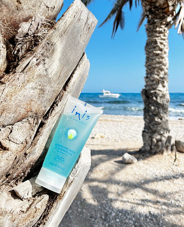 Tube of Inis shower gel on a beach with palm trees and ocean in the background