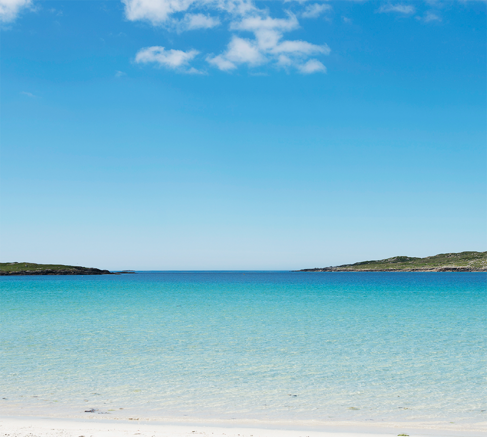 Clear blue sky over a calm turquoise sea with a distant island, Dogs bay Ireland