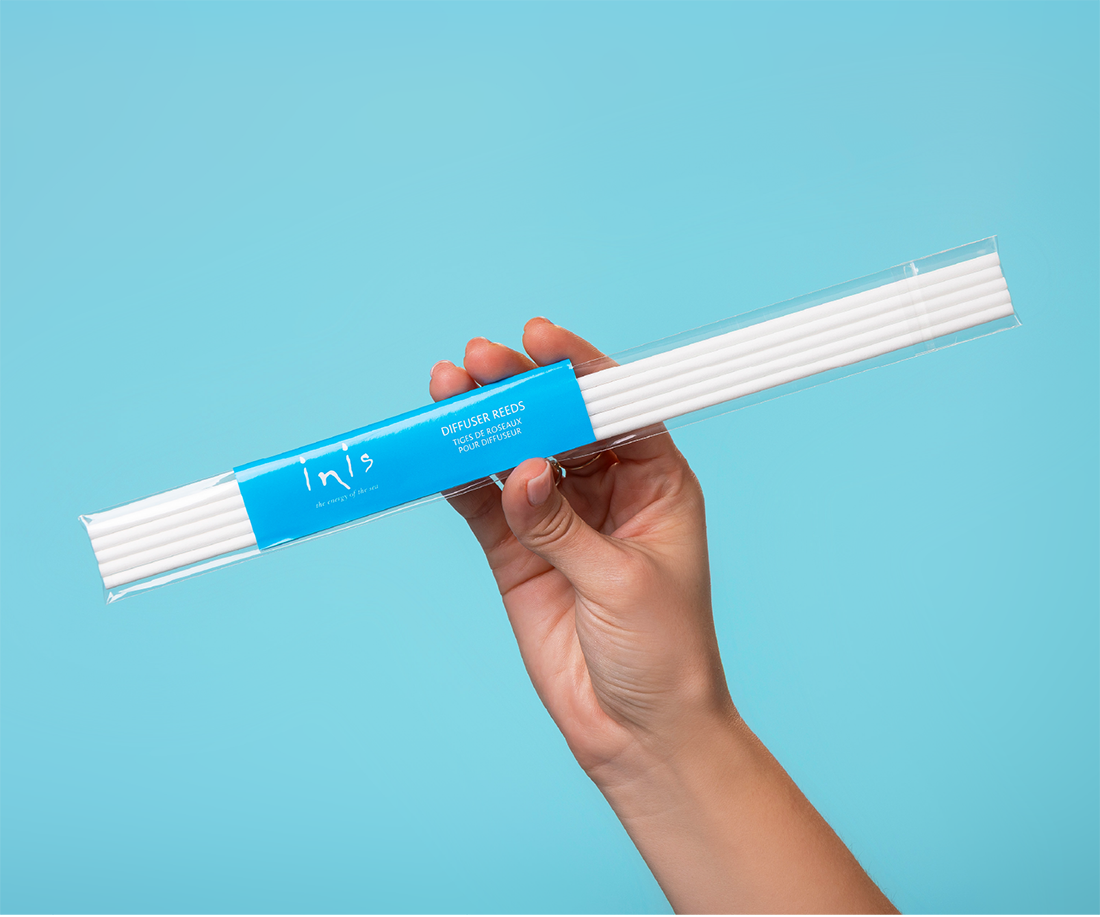 Hand holding a package of white Inis reeds against a blue background
